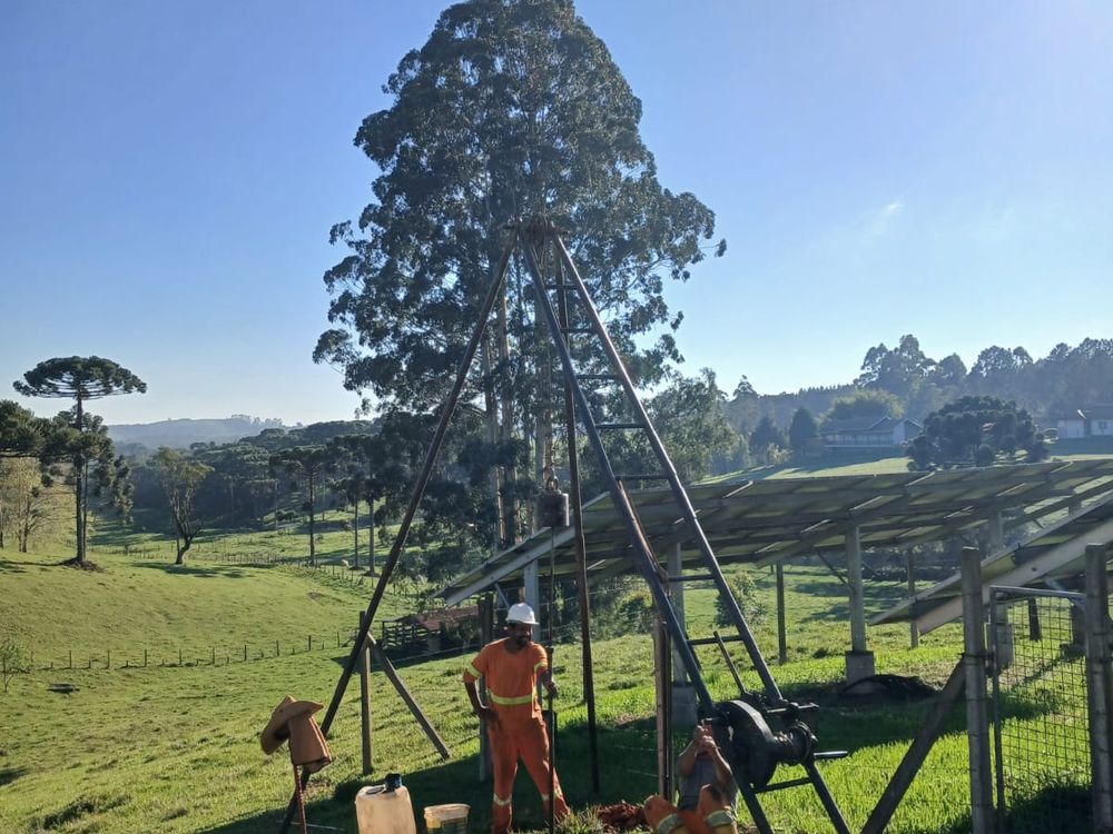 Equipe do Grupo NEV com tripé de perfuração em terreno rural do planalto, com araucárias ao fundo